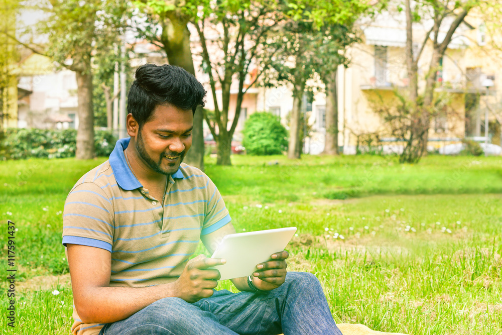 Fototapeta premium Young indian man having video call on tablet in park university