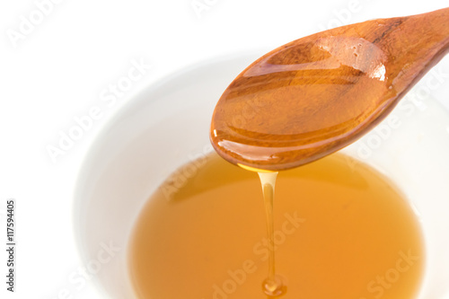 Closeup honey dripping from a wood spoon to bowl on white background  Healthy and beauty spa concept