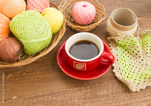 Balls of colorful yarn for crochet. Sample knit. Red Cup with coffee. On wooden background. 