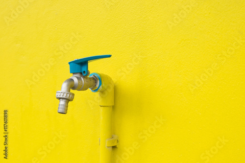 Closeup faucet on concrete Yellow wall background. Water leaking