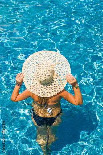 Young woman in bikini wearing a straw hat at the pool