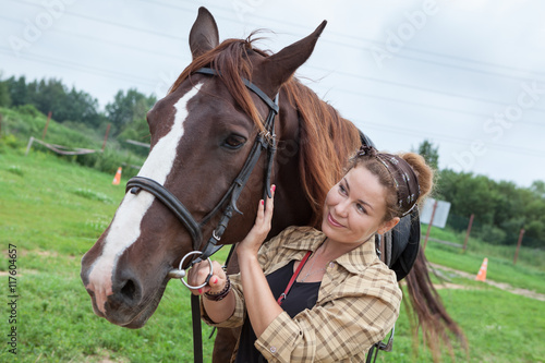 Happy smiling young beautiful woman is near a chestnut horse