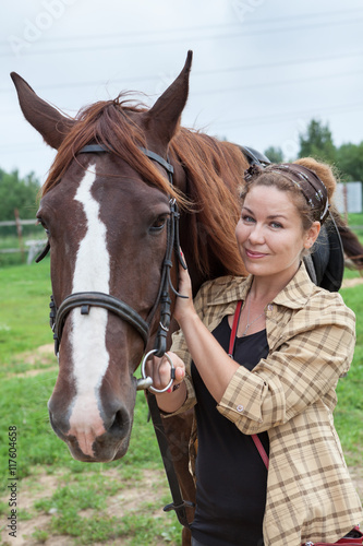 Happy young beautiful woman touching muzzle of chestnut horse