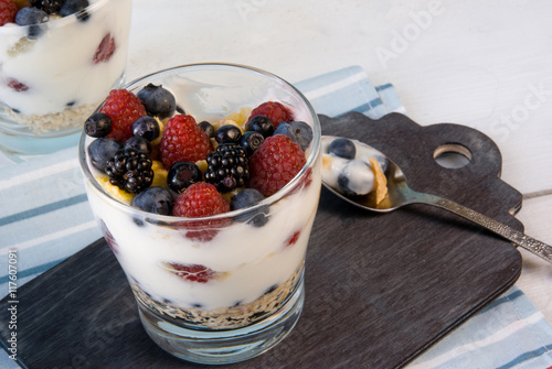 Easy summer dessert: cereal, oatmeal, fruit, yogurt. Dessert tasted: a spoon full of it. Plate with berries in the background. Rustic table and style. Close view.