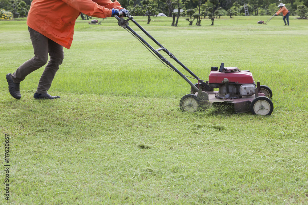 worker and lawn mower working in green grass field worker and lawn mower working in green grass field