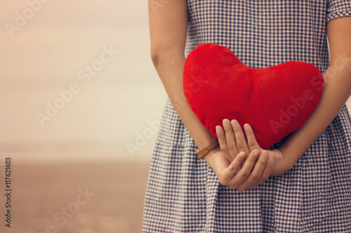 Woman holding a red heart on the beach