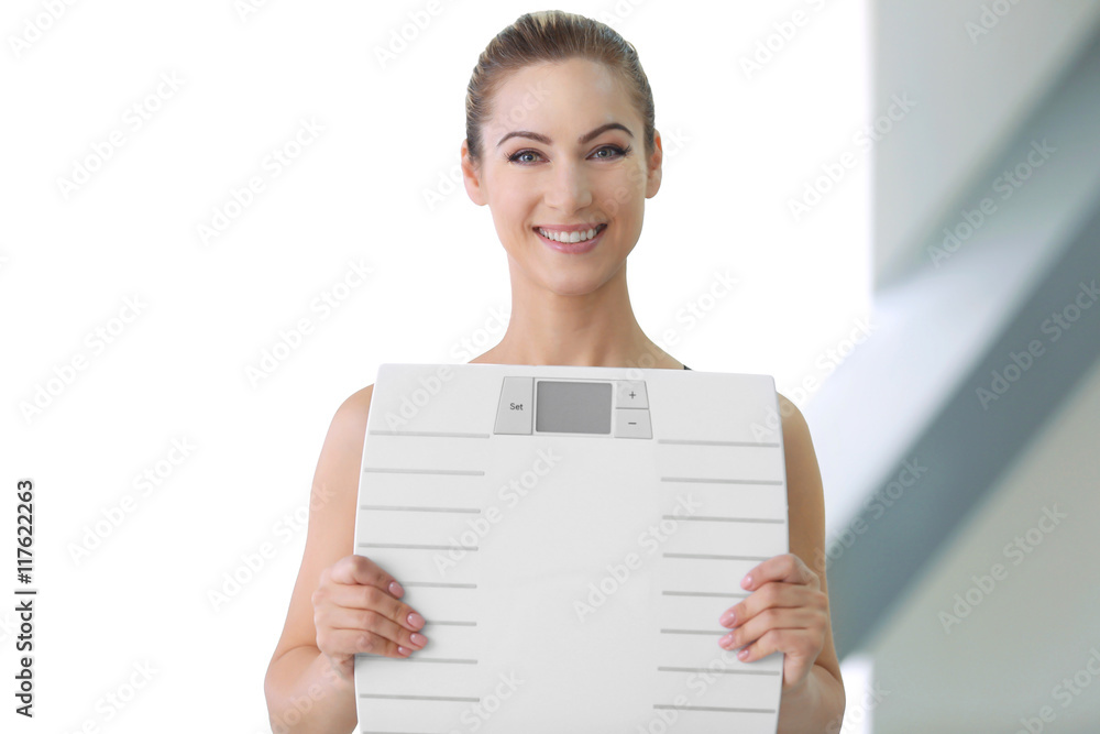 Beautiful young woman holding floor scales on light background Beautiful young woman holding floor scales on light background