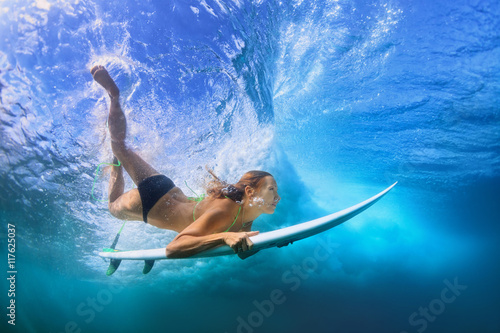 Φωτογραφία Young active girl in bikini in action - surfer with surf board dive underwater under breaking big ocean wave