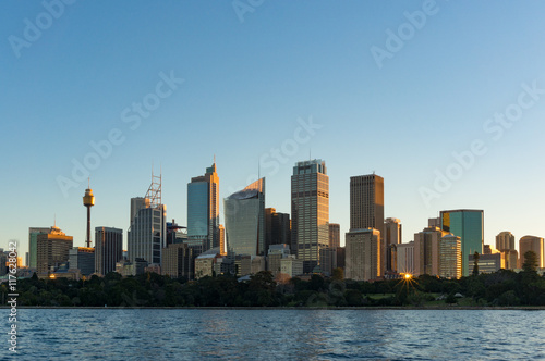 Sydney CBD skyscrapers with Sydney Tower and Royal Botanic Garden view on sunset with sun reflecting from windows. Modern urban cityscape with office buildings © Olga K