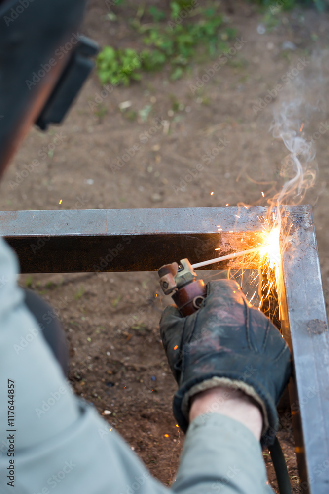 Worker in protective mask welding steel railings outdoors