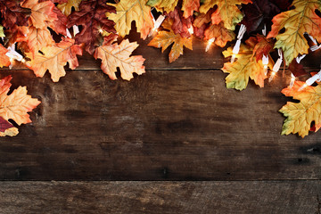 Rustic fall background of autumn leaves and decorative lights over a rustic background of barn wood. Image shot from overhead.