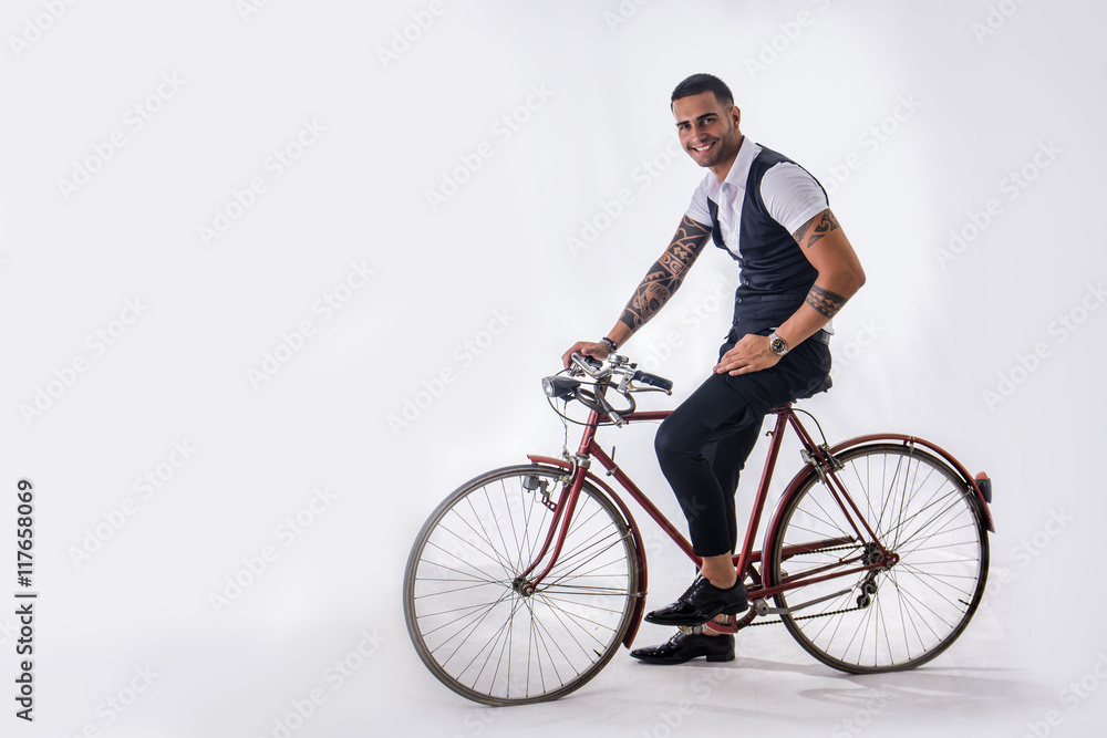 Portrait of young tattooed man in elegant clothes and shoes riding a bicycle.Isolate.Studio shot. Portrait of young tattooed man in elegant clothes and shoes riding a bicycle.Isolate.Studio shot.