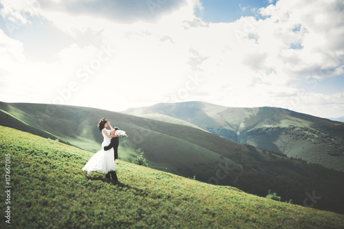 Beautiful fabulous happy bride and stylish groom posing on the background of the sunny stunning mountains
