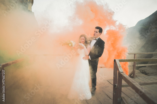 Wedding couple posing near rocks with colored smoke behind them