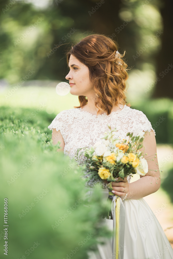 Beautiful brunette bride in elegant white dress holding bouquet posing neat trees Beautiful brunette bride in elegant white dress holding bouquet posing neat trees