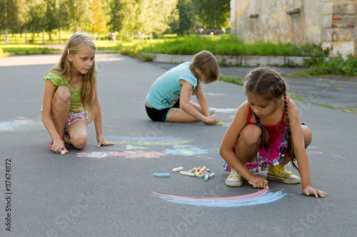 Three girl kids absorbedly drawing chalks on the pavement photo