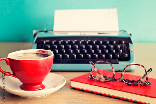 Turquoise typewriter, coffee cup and eyeglasses over red notebook