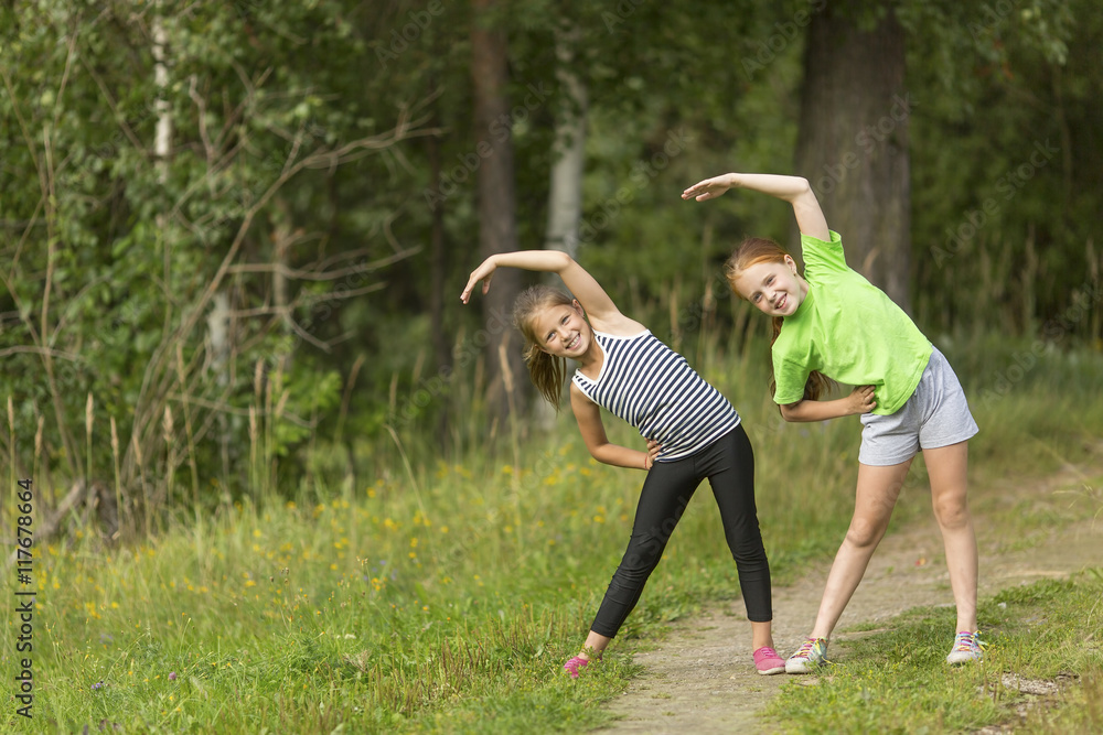Two little cute girls warming up outdoors. Morning exercises. Two little cute girls warming up outdoors. Morning exercises.