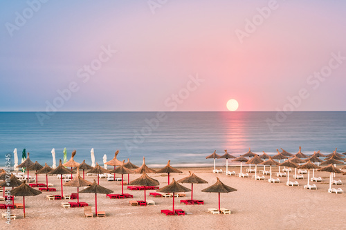 Clear sky sunrise over a sandy Black Sea beach, with straw umbrellas, in Romania photo