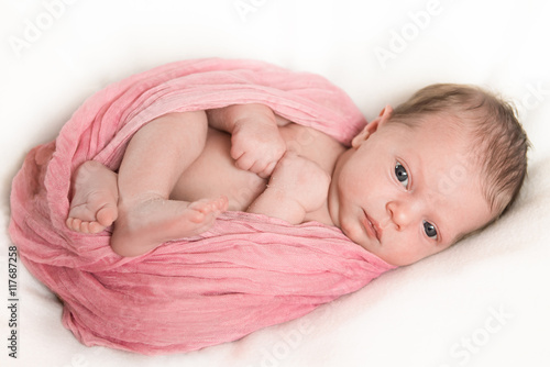 Newborn baby looks under a knitted pink blanket. Close-up photo