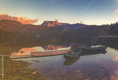 łódki zacumowane przy drewnianym pomoście nad pięknym,górskim jeziorem,kolorystyka retro 