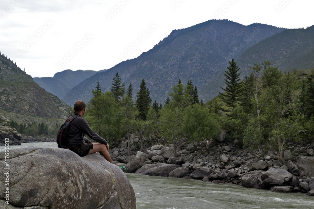 man sitting on a large rock over mountain river