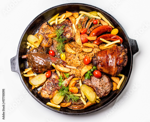 Meat assortment on a large frying pan, potato slices and braised cabbage. On a white background