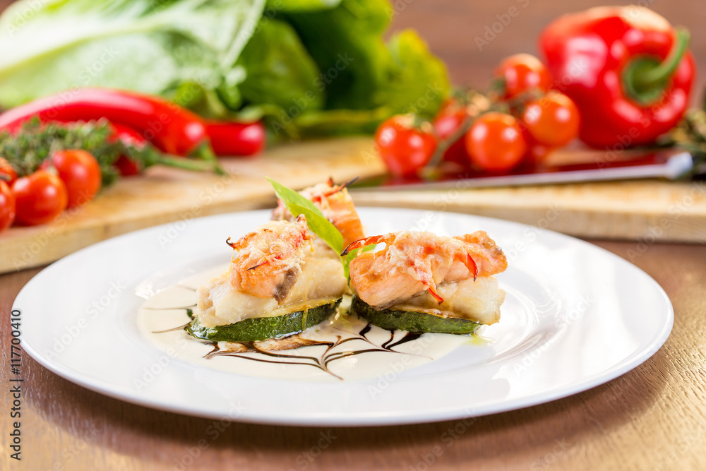Fried zucchini with slices of fish. On a white plate and wooden table Fried zucchini with slices of fish. On a white plate and wooden table