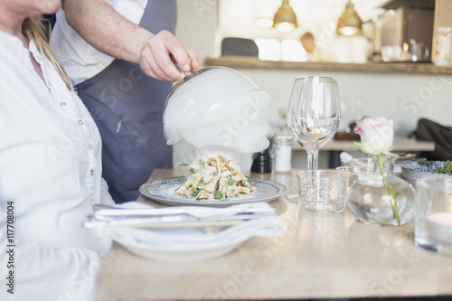 Midsection of waiter lifting cloche from dish for customer in restaurant photo