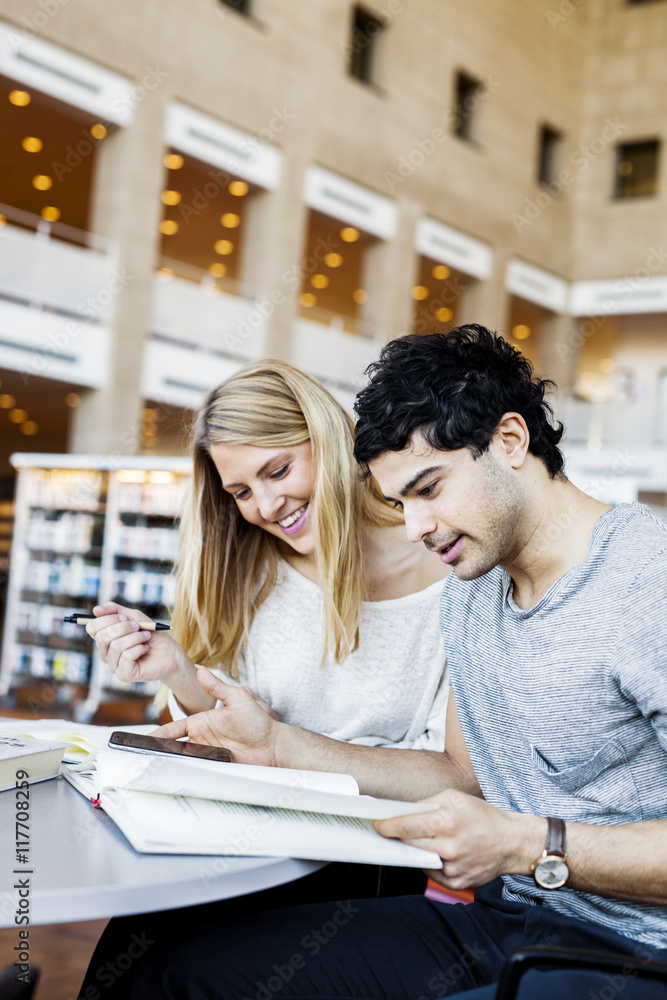 Happy young friends with mobile phone reading notes in library Happy young friends with mobile phone reading notes in library