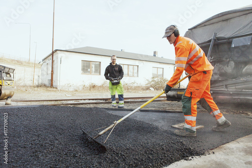 Full length of manual worker with rake spreading asphalt on street photo