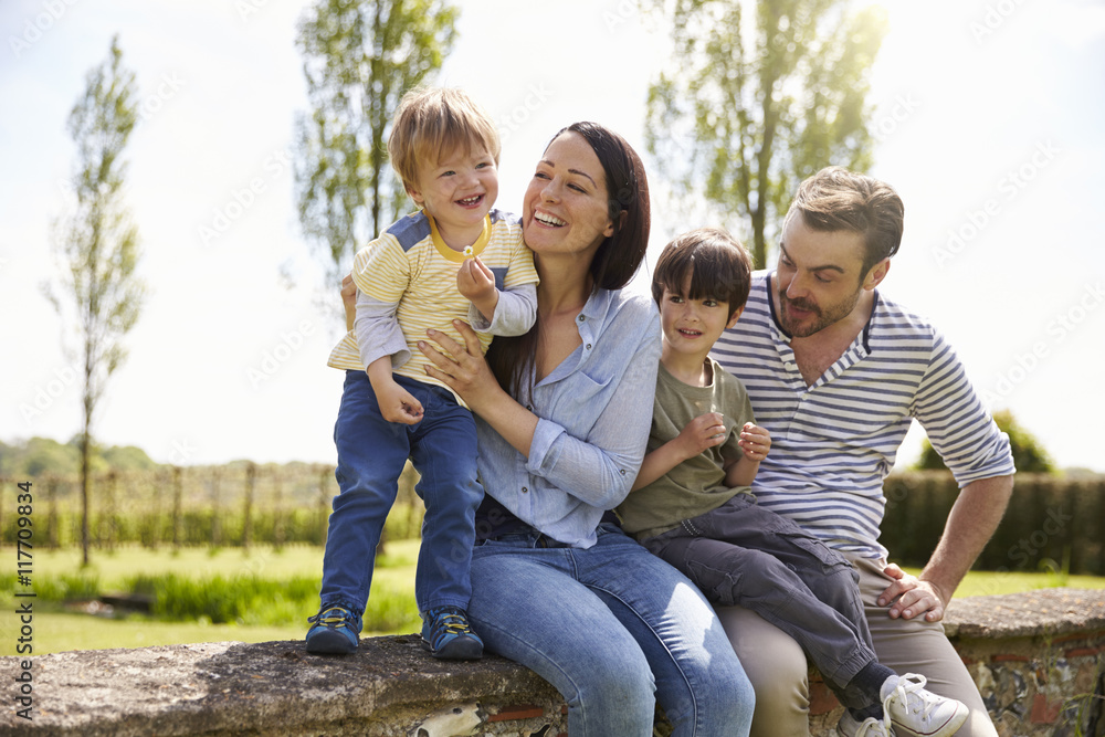 Family Sitting On Wall During Walk In Summer Countryside Family Sitting On Wall During Walk In Summer Countryside