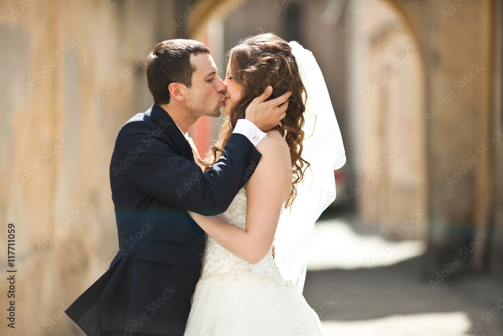 Groom holds bride's head kissing her in the alley