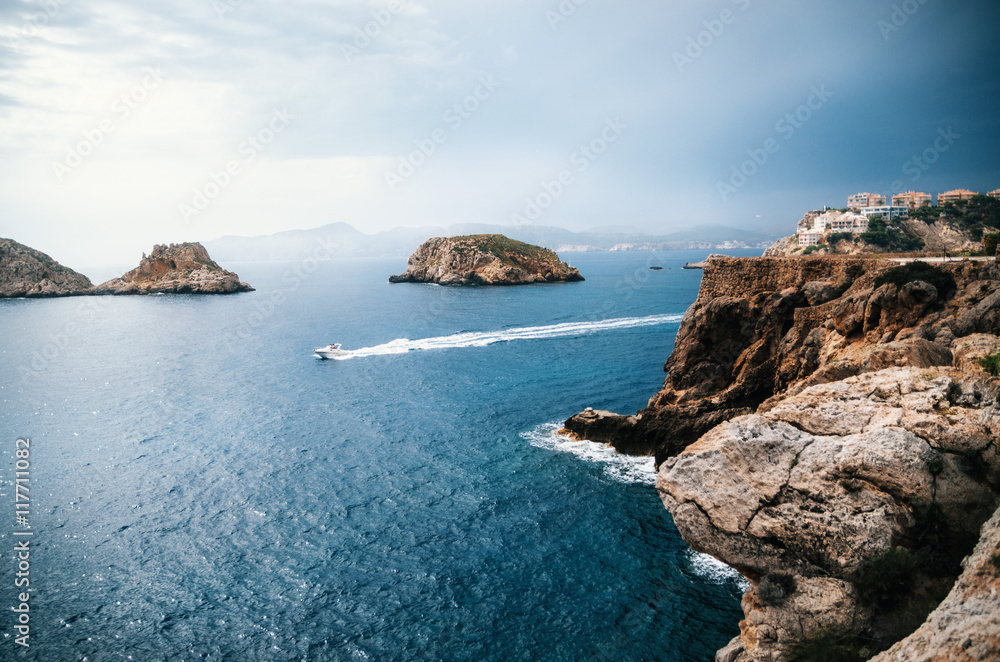 The yacht sails near the rocks of Santa Ponsa in the mediterranean sea before the storm, Mallorca Island