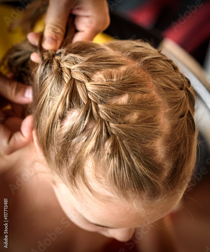 Mother is making of braids on little daughter's head.