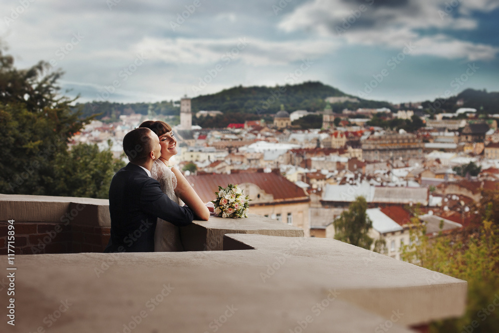 Groom kisses smiling bride from behind standing on the balcony Groom kisses smiling bride from behind standing on the balcony
