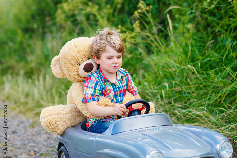 Little kid boy driving big toy car with a bear, outdoors. Little kid boy driving big toy car with a bear, outdoors.