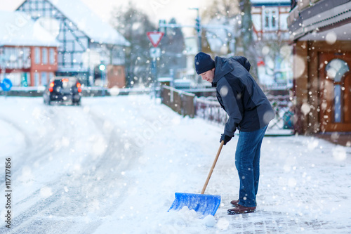 Man with snow shovel cleans sidewalks in winter