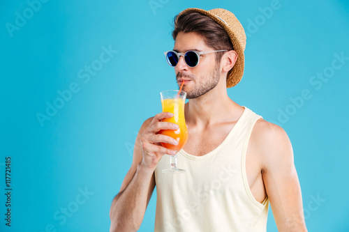 Handsome man in hat and sunglasses drinking fresh orange juice