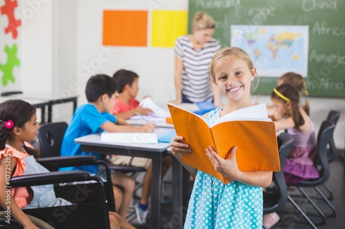 School girl holding a book in classroom