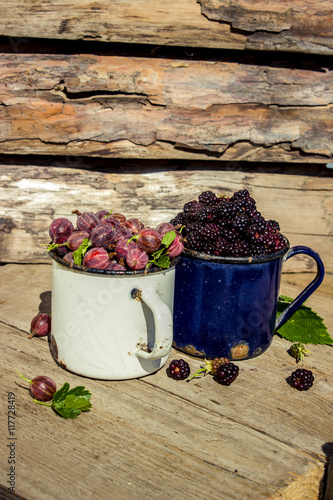 Ripe blackberries and gooseberries in a metal mug on a wooden background closeup. Rustic style, selective focus.  photo