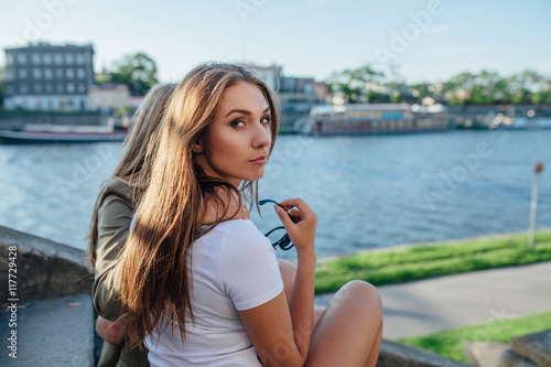 Two young girls sitting on the stairs next to the river and hugg