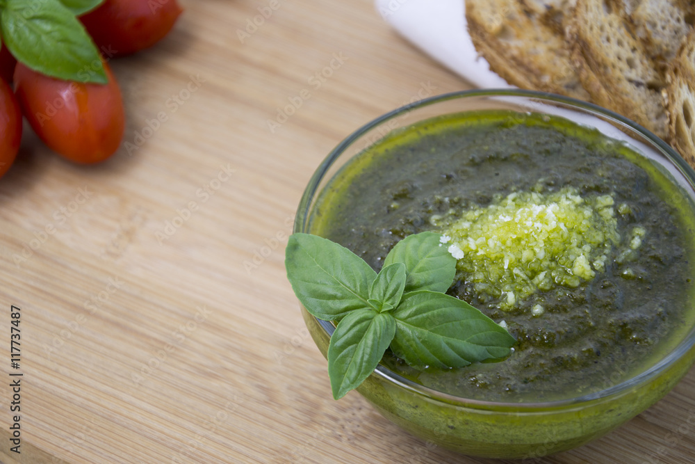 Green pesto with fresh basil leaves in small glass bowl on wooden background Green pesto with fresh basil leaves in small glass bowl on wooden background