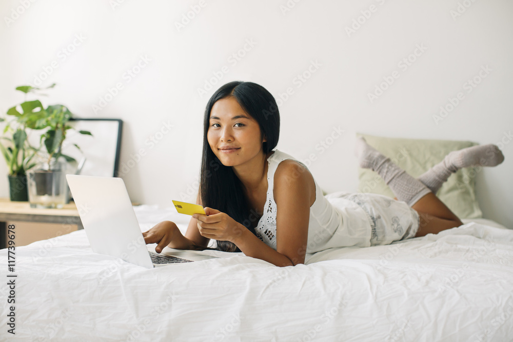 Young woman lying in bed shopping online Young woman lying in bed shopping online