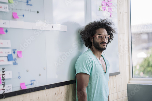 Young creative proffessional leaning against white board in office photo