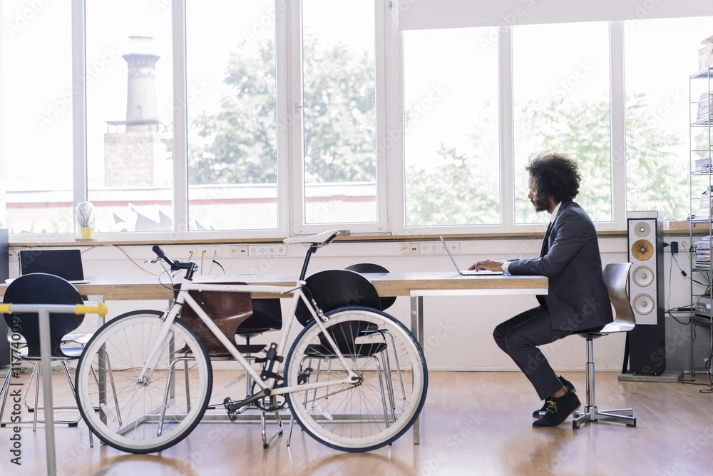 Young businessman working in office with bicycle leaning against desk Young businessman working in office with bicycle leaning against desk