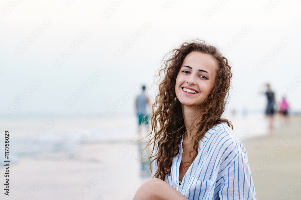 Beautiful woman sitting on beach in white shirt, smiling