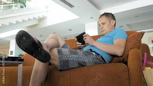 A man is shown enjoying on a couch working on his mid pad. Tablets made a remarkable change in the tech industry. Extremely portable and has a good battery life. photo