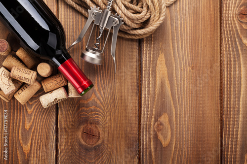 Red wine bottle, corks and corkscrew over wooden table backgroun