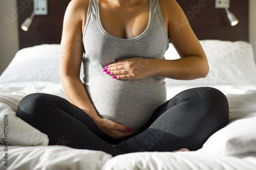 Pregnant woman sitting on bed with her hand at belly